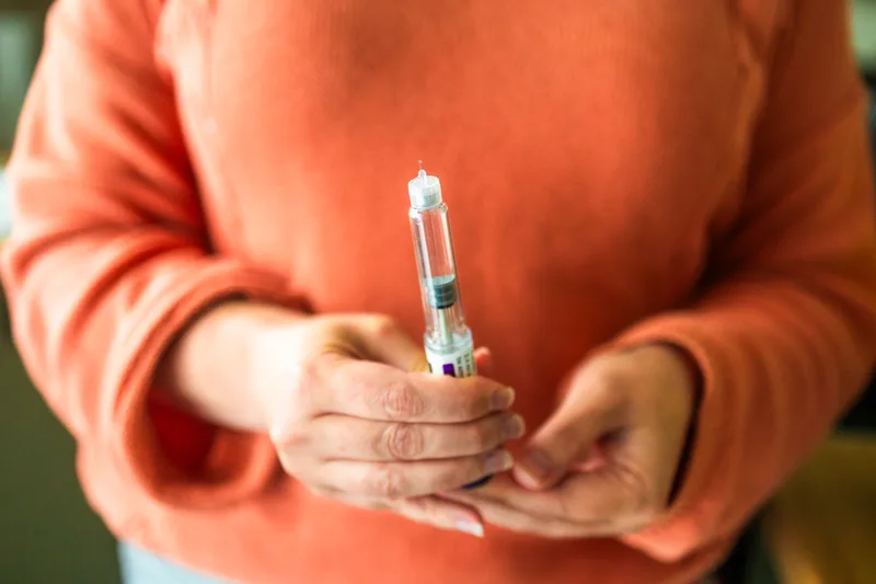 A person in an orange sweater holds a prescription injection pen in both hands