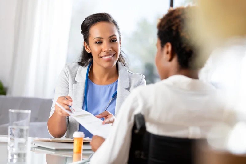 A clinician hands a printed lab report to a patient across a desk and explains it