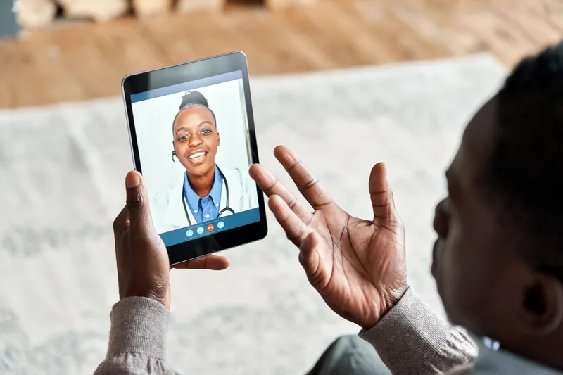 A man at home gestures while talking with a doctor over a video call on his tablet