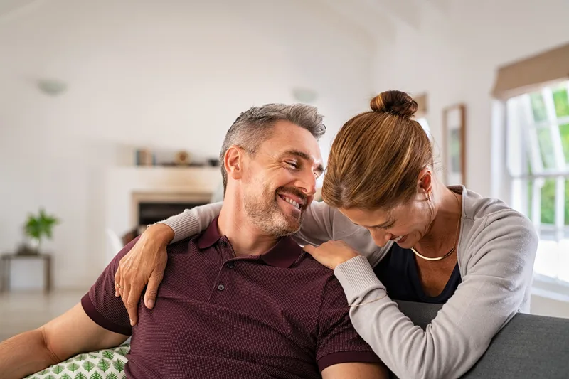 A middle-aged couple laughing together on a sofa at home