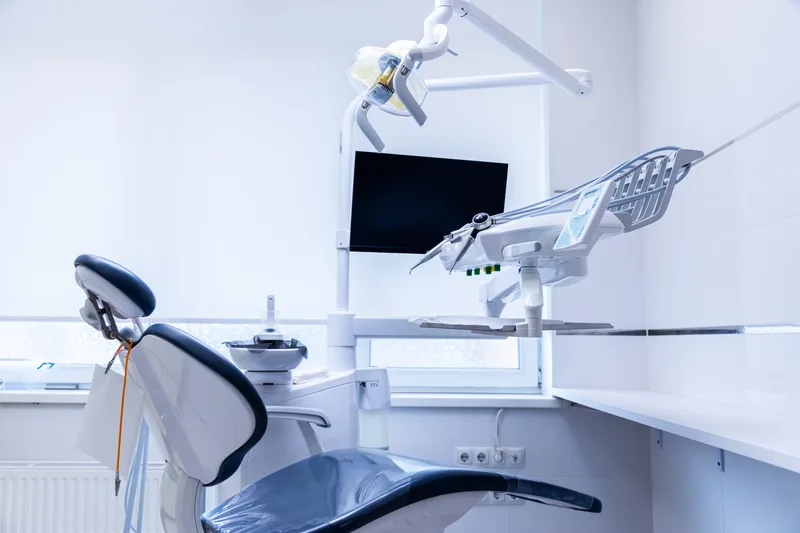 A bright, empty treatment suite with a reclining chair, overhead light and monitor