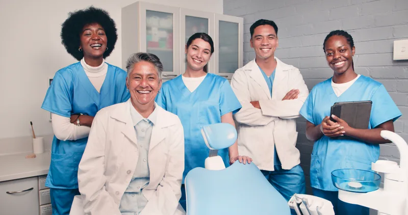 Dentists and assistants gathered around a dental chair, smiling at the camera