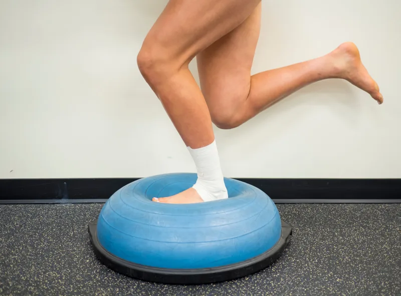 Athlete with a taped ankle balancing on one foot on a balance trainer