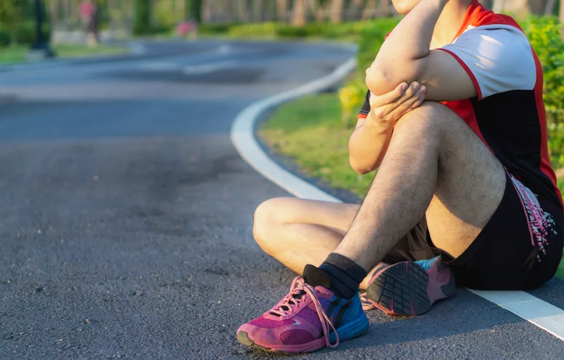 Athlete sitting by a road holding a sore elbow