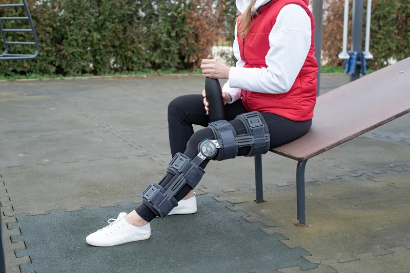 Woman in a hinged knee brace resting on an outdoor bench
