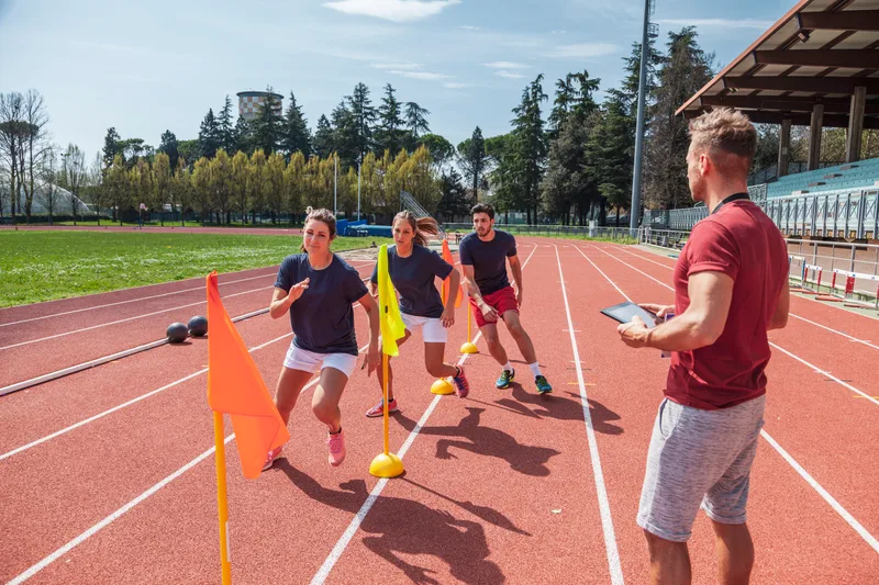 Athletes doing agility drills on a running track while a coach records results on a tablet