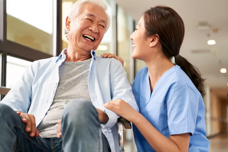 A care aide and an older man laugh together in a common room