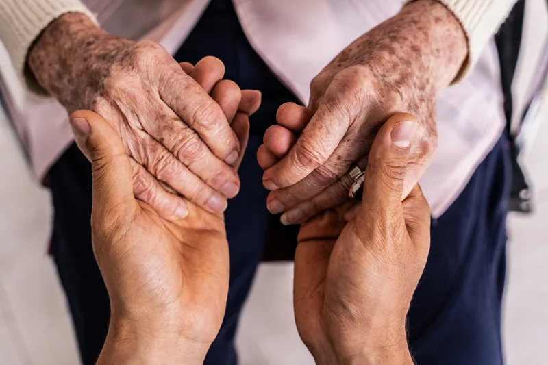 Close view of a younger person's hands holding an older person's hands