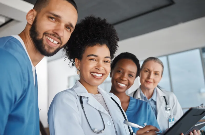 Four smiling members of a clinic care team in white coats and scrubs standing close together