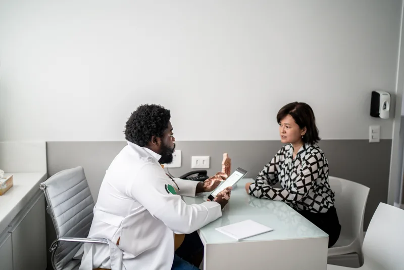 Doctor going over notes with a midlife woman across a desk in a quiet consult room