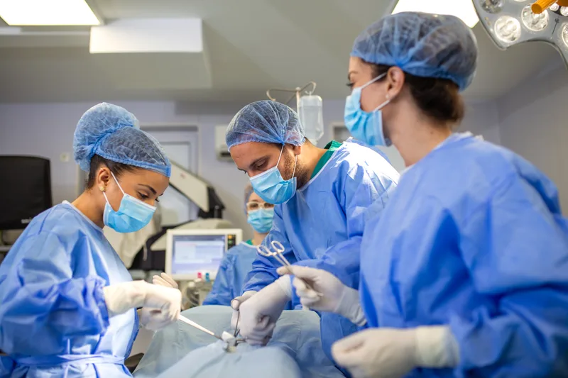 Surgical team in caps, masks and blue gowns working together in an operating room