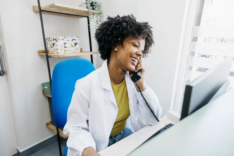 A smiling front desk team member on the phone at a bright reception desk