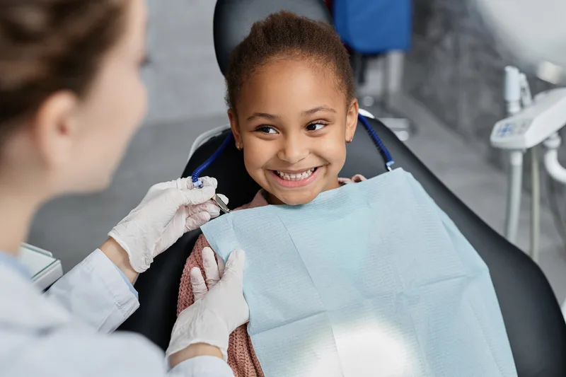 A smiling girl in a dental chair with a hygienist beside her