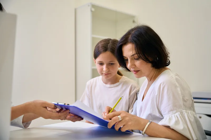 A mother and her daughter filling in a form together at a clinic desk