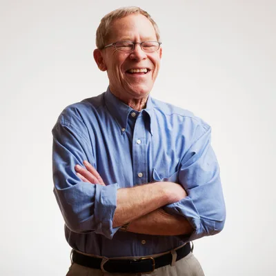 A smiling man in his seventies with glasses and a blue shirt