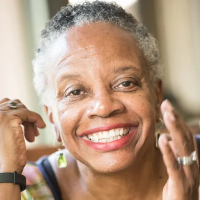 A woman in her sixties laughing with her hands raised near her face