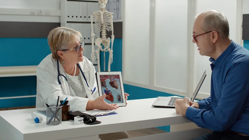 A doctor points to a heart-anatomy diagram on a tablet while a patient follows along