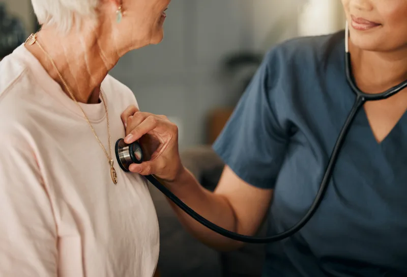 Close-up of a clinician resting a stethoscope on an older woman's chest during a check-up