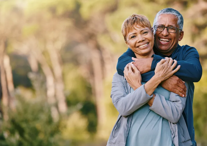 A couple in their sixties hug and laugh together on an evening walk outdoors
