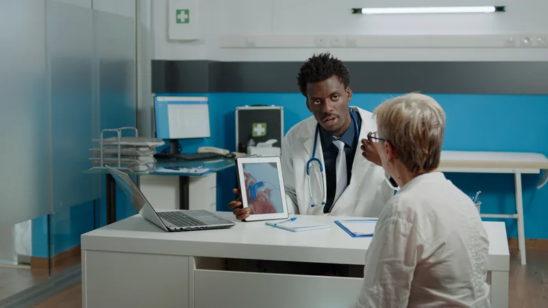 A physician holds up a tablet showing a heart scan to explain findings to an older patient