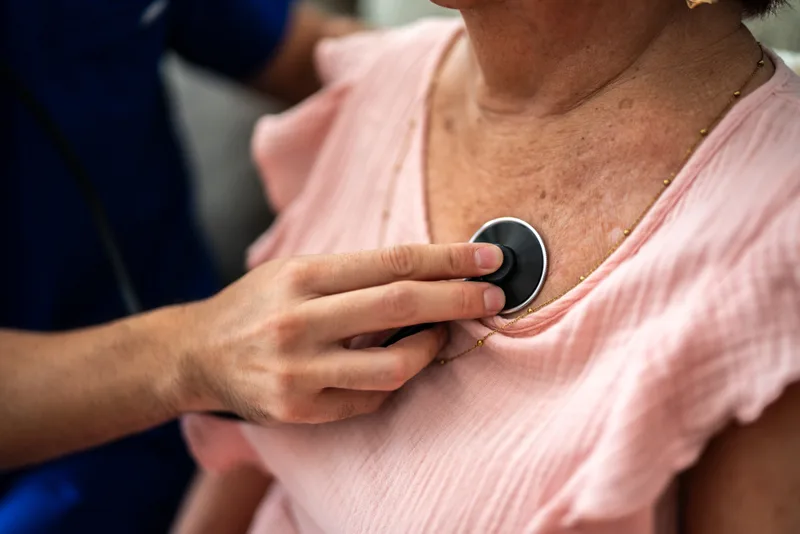 Close-up of a hand placing a stethoscope on a patient's chest to listen to the heart