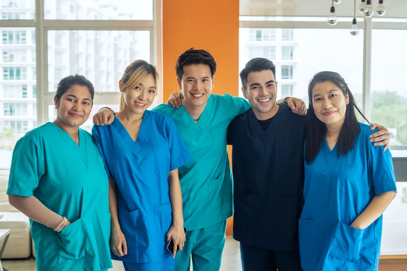 Five smiling members of a clinic care team in scrubs standing together