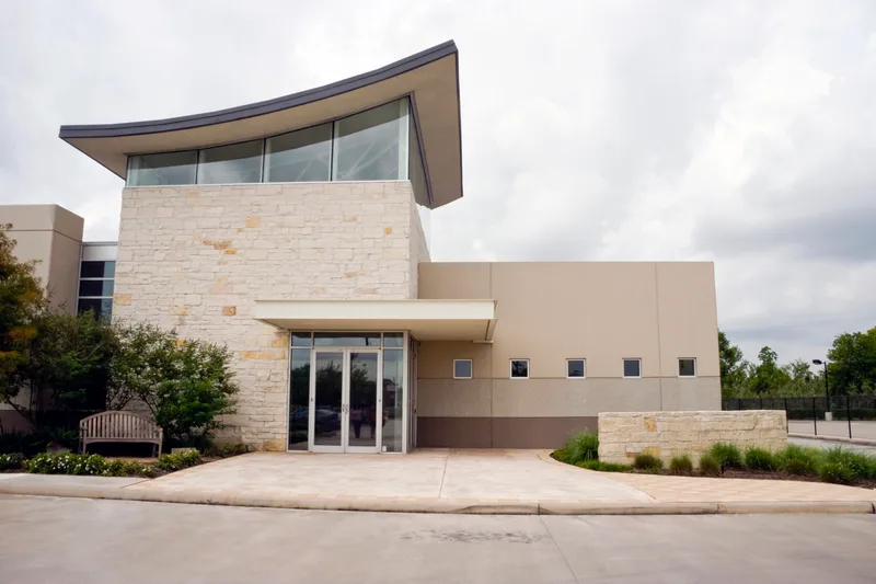 Modern stone and glass clinic building with a curved roof and a landscaped entrance