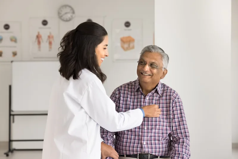Family doctor listening to an older man's heart with a stethoscope in a bright exam room