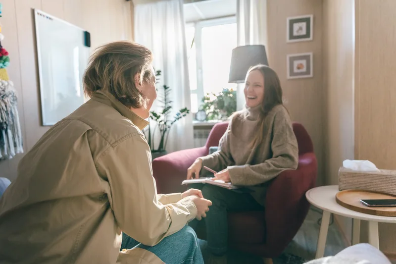 A clinician and a patient share a light moment in a warm, plant-filled office