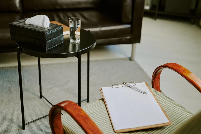 A quiet consultation room with a soft armchair, a side table with tissues and a glass of water, and a clipboard on the seat