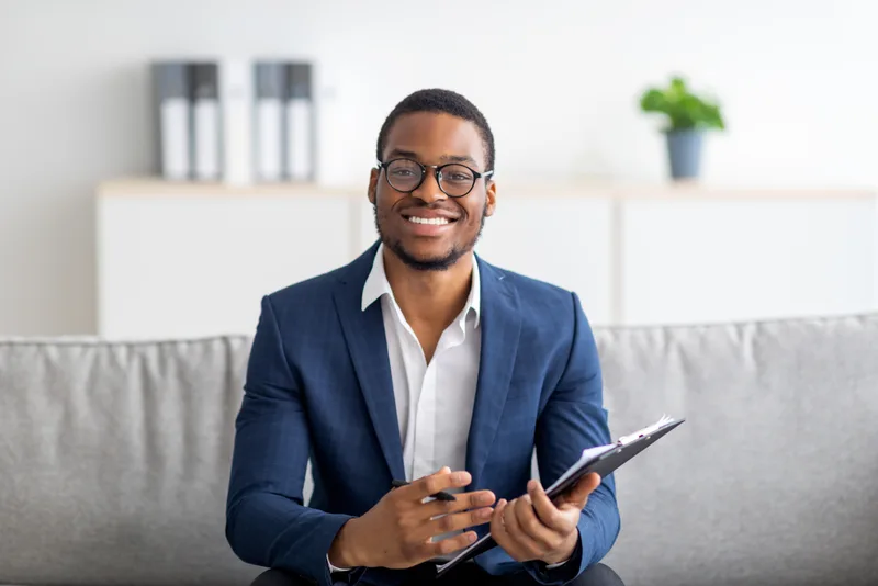 Dr. Daniel Osei, a child and adolescent psychiatrist in a navy blazer, smiling on an office sofa