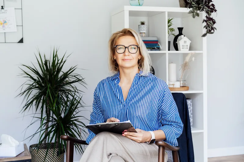 Dr. Helen Marsh, a psychiatrist in her fifties with glasses, smiling in her office