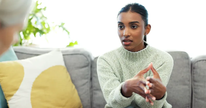 A woman in a sage sweater sits on a sofa and explains how she has been feeling