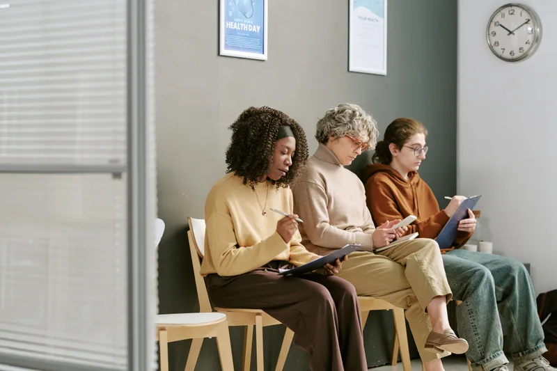 Three people fill out intake forms on clipboards in a calm waiting room