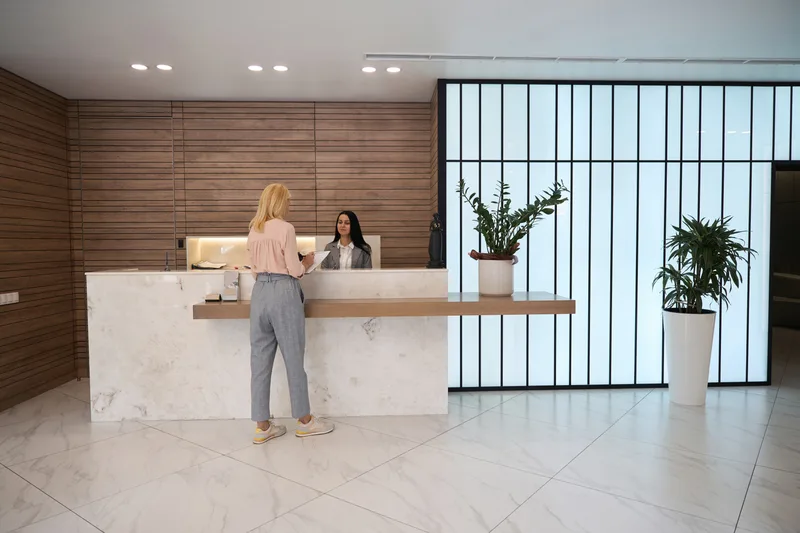 A calm practice lobby with a marble front desk, warm wood walls and tall plants