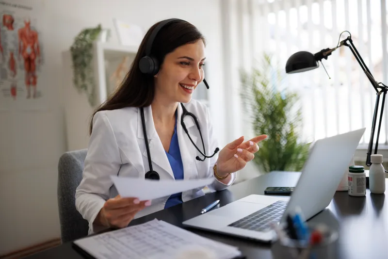 A clinician smiles while talking with a patient on a video call at her laptop