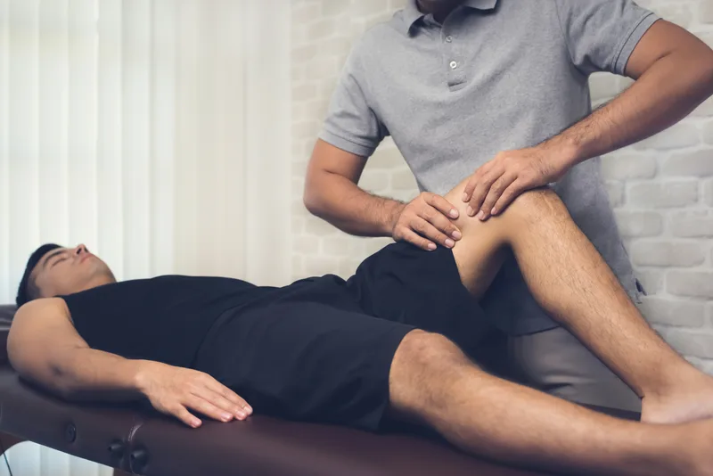 Physical therapist assessing the bent knee of an athlete lying on a treatment table
