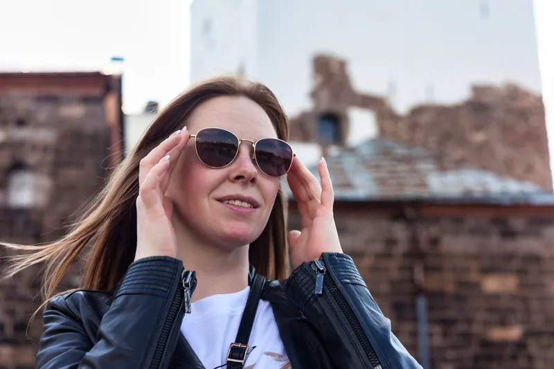 A woman smiling as she adjusts her sunglasses on a bright day outdoors