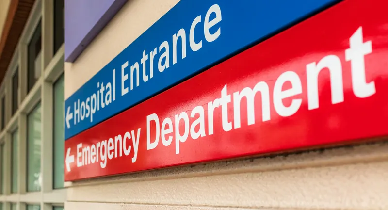 Red Emergency Department wayfinding sign with a directional arrow beside the blue hospital entrance sign