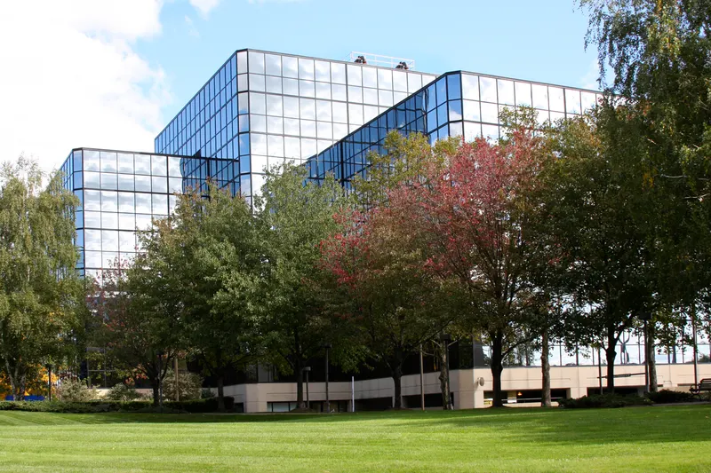 Mirrored-glass hospital building at Riverbank East reflected among mature trees and a broad green lawn