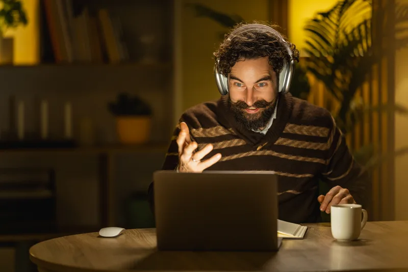 A man wearing headphones at his desk in the evening, mid-conversation in an online session