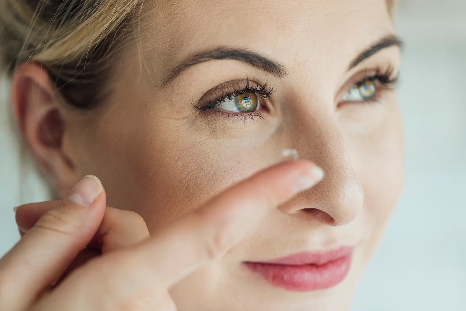 A close-up of a woman balancing a soft contact lens on her fingertip as she raises it toward her eye