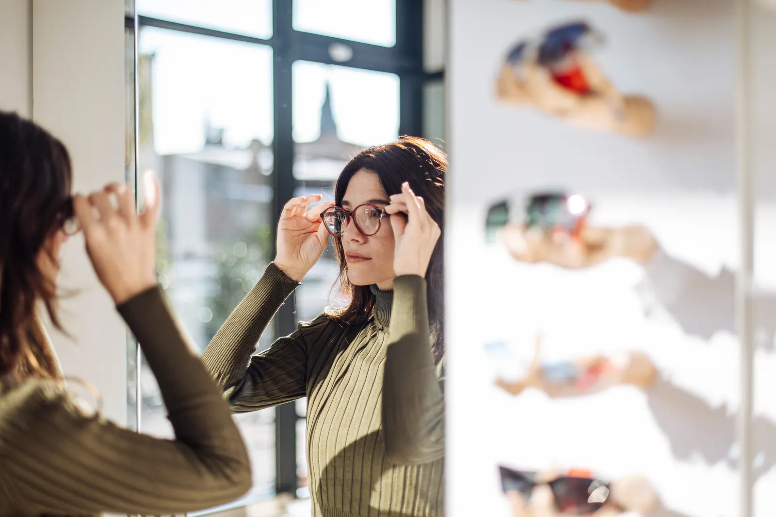 A customer trying on a round acetate frame in front of a mirror in the sunlit Sightline dispensary