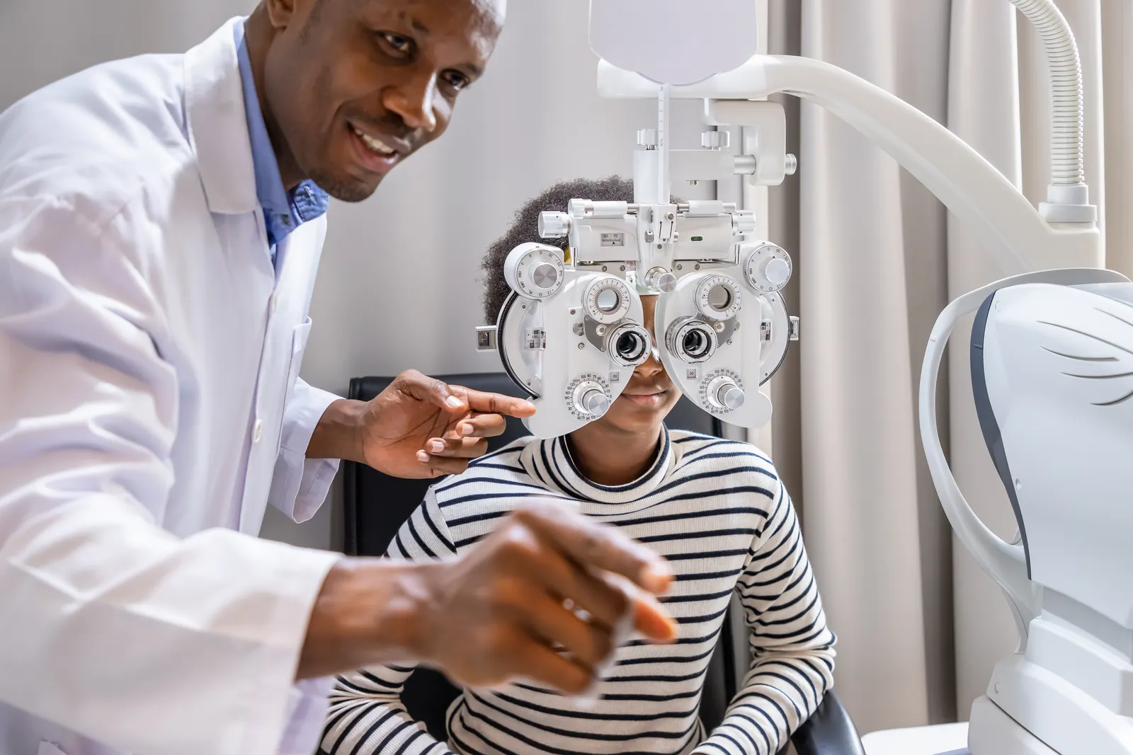 An optometrist adjusting a phoropter in front of a patient during the refraction part of an exam