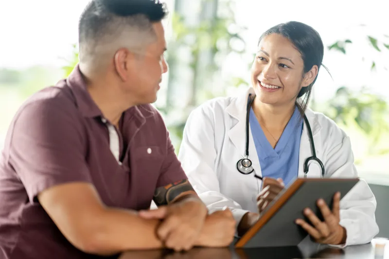 A smiling clinician reviews results on a tablet with a patient at a table