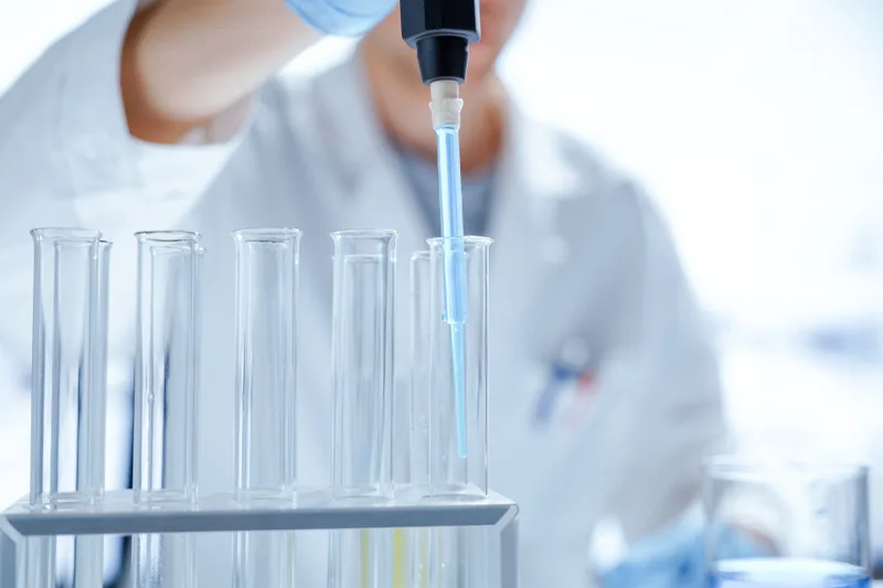 A lab technician pipettes a sample into a row of clear test tubes