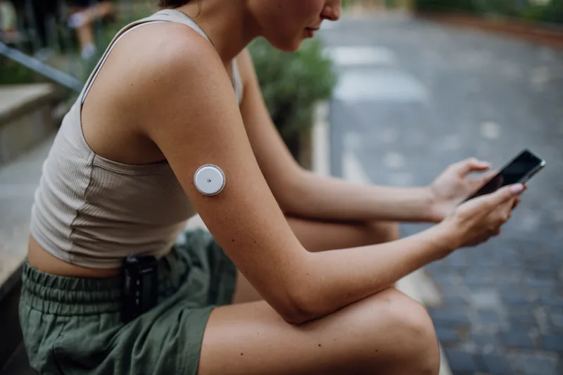 A woman with a glucose sensor on her upper arm checks the reading on her phone