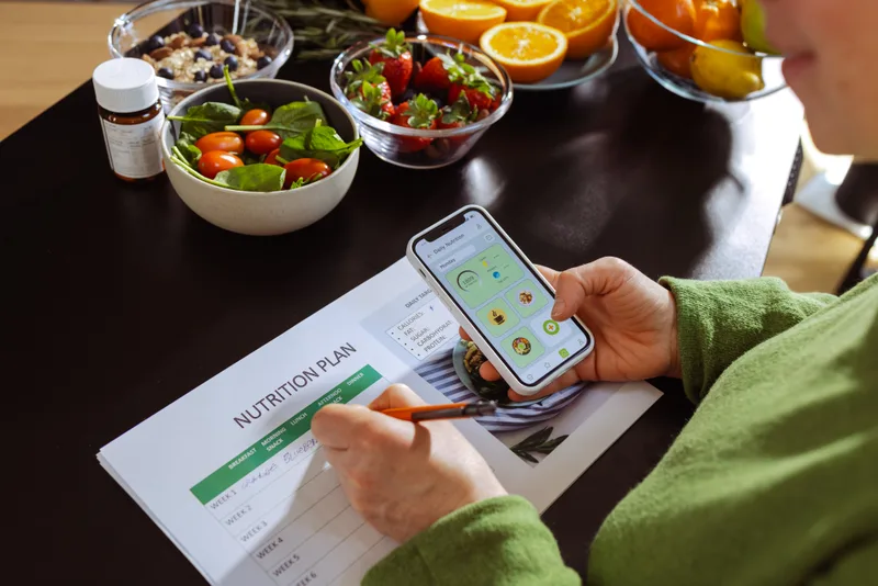 Someone fills in a weekly nutrition plan beside bowls of salad, berries and fruit