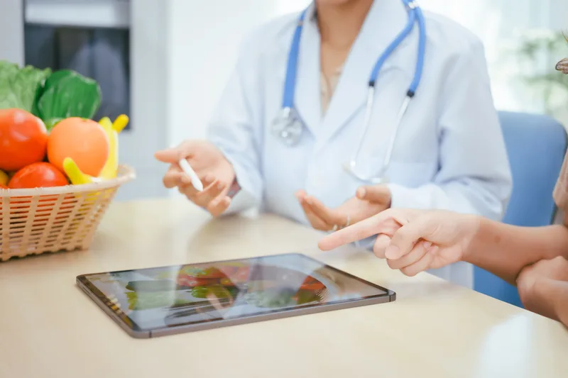 A clinician talks through a food plan on a tablet next to a basket of fresh vegetables