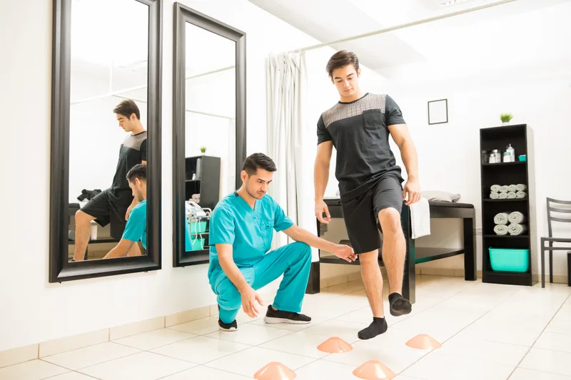 Athletic therapist coaching a patient through an agility-cone stepping drill in a rehab gym